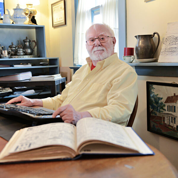Harry Bellangy seated at his computer surrounded by historic artifacts and paperwork